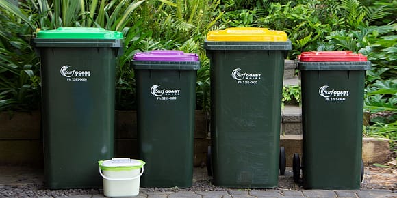 A line up of bins in a local Australian council, there’s a green lid, purple lid, yellow lid and red lid.
