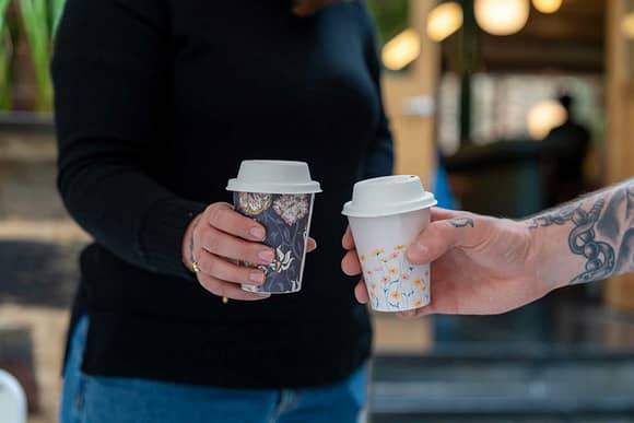 Close up of two people holding a takeaway coffee cup in their hands.