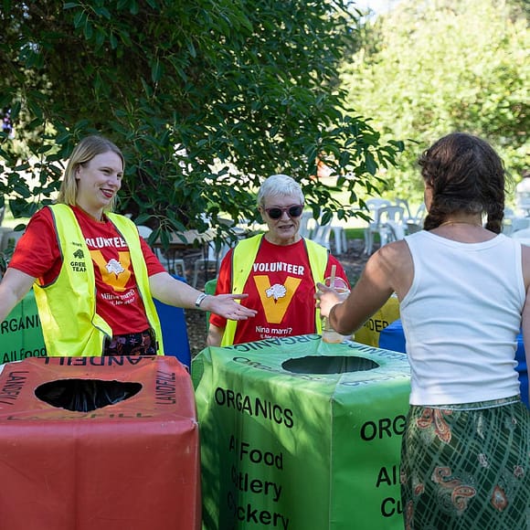 Two volunteers helping a festival goer dispose of her clear bioplastic cup and paper straw.