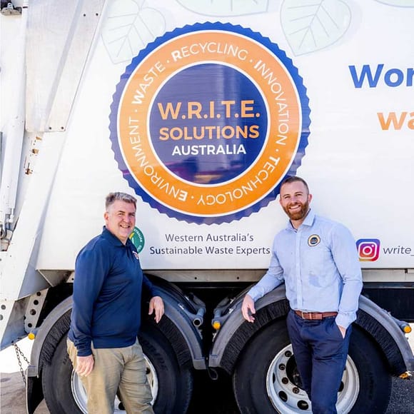 Two W.R.I.T.E. Solutions employees standing in front of their white waste collection truck with a big orange and blue W.R.I.T.E. Solutions logo on it.